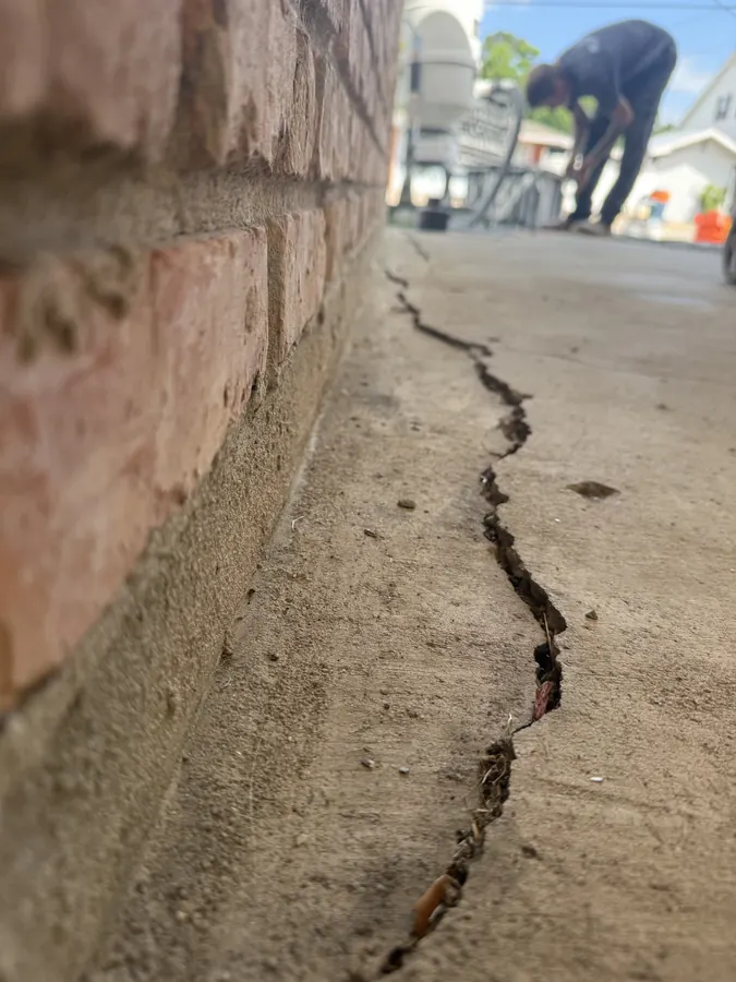 Cracked residential slab along a brick wall before repair